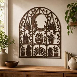 May include: A dark brown, arched wall hanging featuring a laser-cut design of various potted plants, hanging planters, and a crescent moon. The intricate lattice structure includes vines and foliage motifs arranged within a grid-like frame.