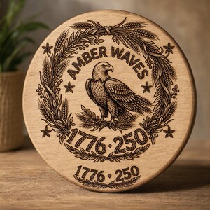 May include: A round wooden plaque with an engraved design. The design features an eagle, wheat stalks, stars, and the words "AMBER WAVES" and "1776-250". The plaque is light brown.