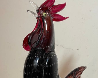 May include: A black and red glass rooster figurine with a clear glass base. The rooster has a textured body and a raised comb and wattle.
