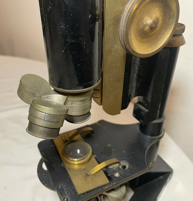 May include: An antique microscope with a black body and brass components. The microscope features multiple lenses, adjustment knobs, and a stage for slides. The design suggests a vintage scientific instrument, likely used for biological or medical research.