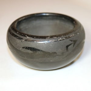 May include: A black ceramic bowl with a geometric design. The bowl is hand-painted with a black and white pattern.