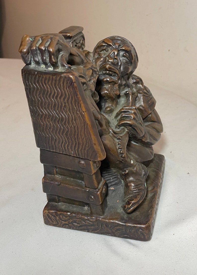 Puede incluir: Una escultura de bronce de un hombre sentado en una silla de madera, sosteniendo una pipa en su mano. La escultura es detallada y realista, con una superficie texturizada.