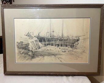 May include: A black and white pencil drawing of a ship on a wooden frame, resting on a beach. The ship has three masts and sails, and there are people working on the ship. The drawing is framed in a brown wooden frame.