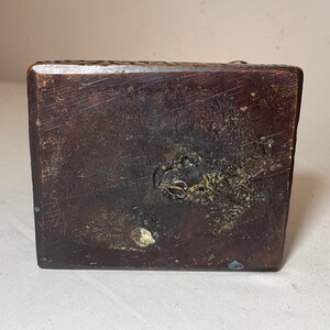 Puede incluir: La parte inferior de una base de madera marr&oacute;n oscuro con un peque&ntilde;o lazo de metal unido a la base.