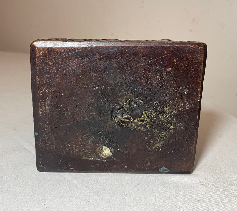 Puede incluir: La parte inferior de una base de madera marr&oacute;n oscuro con un peque&ntilde;o lazo de metal unido a la base.