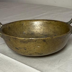 Puede incluir: Una taza de cer&aacute;mica blanca con asa negra y el texto "But First, Coffee" en negrita negra. La taza se encuentra sobre un fondo borroso, sugiriendo un ambiente acogedor.