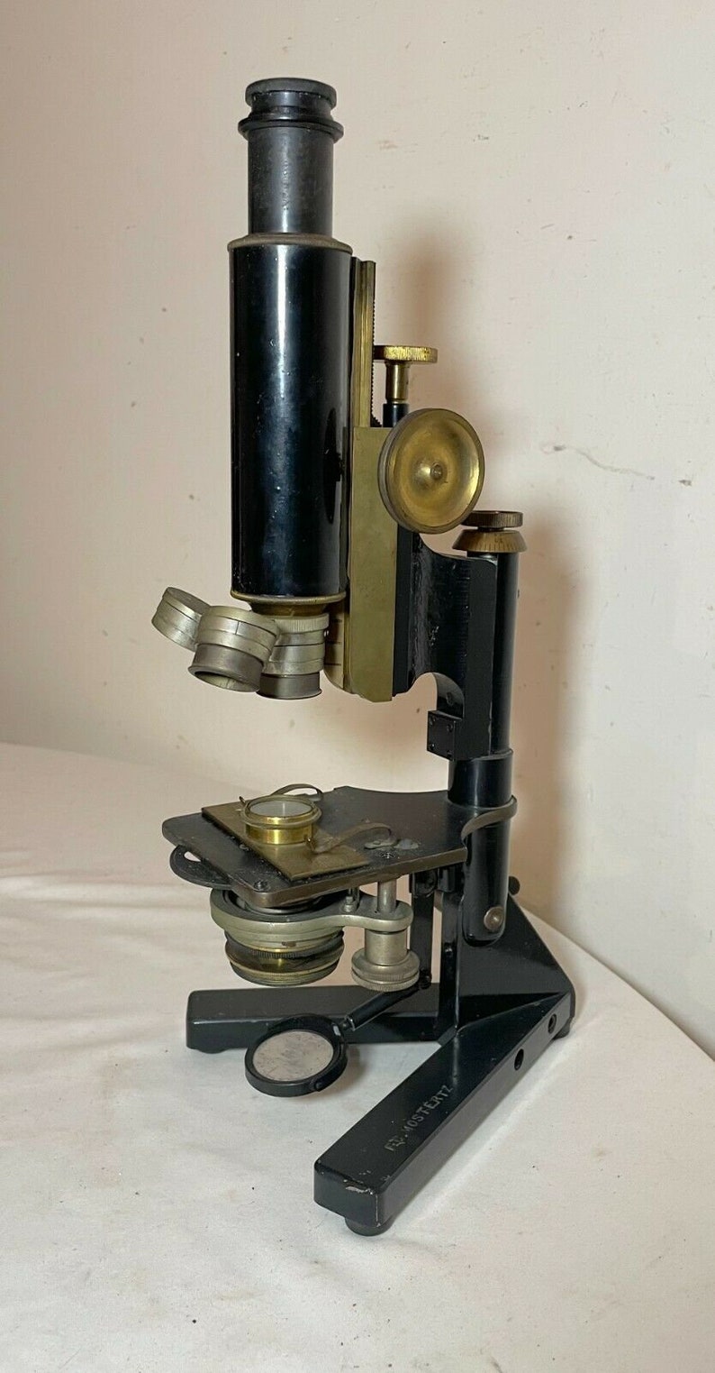 May include: An antique microscope with a black body and brass accents. The microscope has multiple lenses, adjustment knobs, and a stage for slides. The base is marked with text. A classic scientific instrument.
