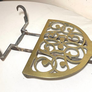 May include: An antique brass and iron trivet. The brass portion is a half-circle with an ornate, openwork design. The iron base has two curved hooks and a support for the brass piece. The trivet is likely used for placing hot items.