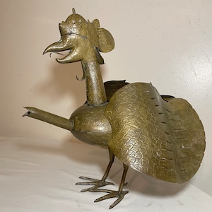 May include: A brass sculpture of a bird with a crown on its head. The bird has detailed wings and a long neck. The sculpture is in a vintage style.