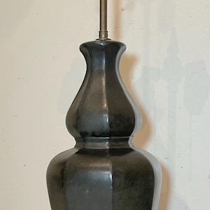 May include: A dark gray table lamp with a double-lobed body and a brass fixture. The lamp sits on a gold and red base. The lamp has two light bulb sockets.