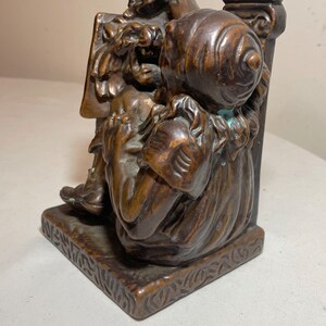 Puede incluir: Un par de sujetalibros de bronce que representan dos figuras, una sentada y la otra de pie, con detalles intrincados y una base texturizada.