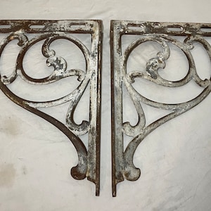 May include: Two antique cast iron shelf brackets with a white painted finish and intricate scrollwork design.