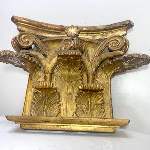 May include: A gold-painted architectural element with ornate carvings. The piece features stylized floral and leaf designs, with a curved top and a rectangular base. The details include scrolled accents and a central star-shaped embellishment. The overall style suggests a classical or antique aesthetic.