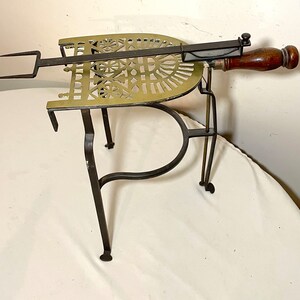 May include: A vintage brass and iron toasting fork stand with a wooden handle. The stand has a decorative, pierced brass top and three legs.