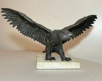May include: A bronze eagle sculpture with outstretched wings, perched on a white marble base.