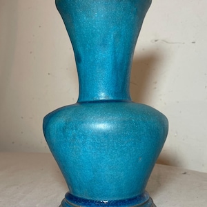 May include: A turquoise ceramic vase with a flared top and a rounded body. The vase has a textured surface and a dark brown base. The vase is approximately 10 inches tall.