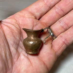 May include: A small, hammered copper pitcher with a curved handle. The pitcher is about 3 inches tall and has a rustic, antique look.