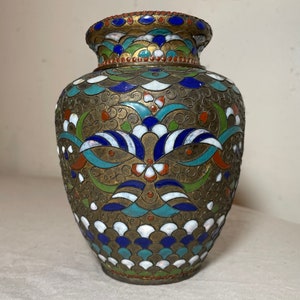 May include: A small, round, gold-colored vase with a decorative design of blue, green, white, and red enamel. The vase has a scalloped rim and a floral pattern.