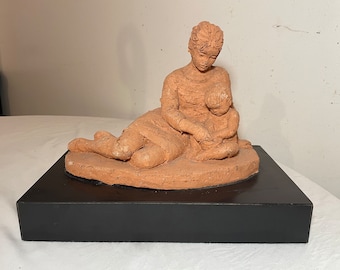May include: A terracotta sculpture of a woman holding a child. The sculpture is on a black base.