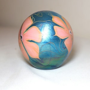 May include: A blue glass paperweight with a pink floral design. The glass has an iridescent finish.