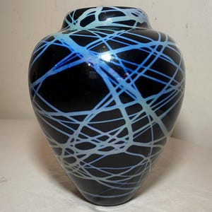 May include: A black glass vase with a white and blue iridescent design. The vase has a rounded body and a narrow neck.