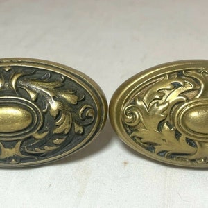 May include: Two antique brass door knobs with an oval shape and intricate floral designs.