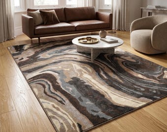 May include: A rectangular area rug featuring a swirling, marbled pattern in shades of dark brown, charcoal grey, cream, and beige. The rug has a low-pile texture and is positioned on a light-toned wooden floor, covering a large portion of the space.