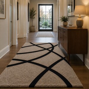 May include: A rectangular area rug featuring a textured beige pile with a bold, black linear pattern consisting of intersecting curved lines that span across the surface, creating a geometric design that covers the length of the hallway floor.