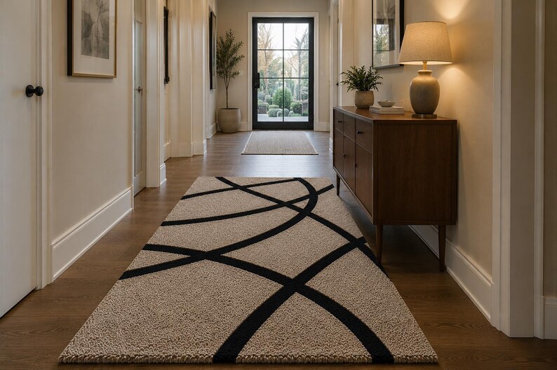 May include: A rectangular area rug featuring a textured beige pile with a bold, black linear pattern consisting of intersecting curved lines that span across the surface, creating a geometric design that covers the length of the hallway floor.