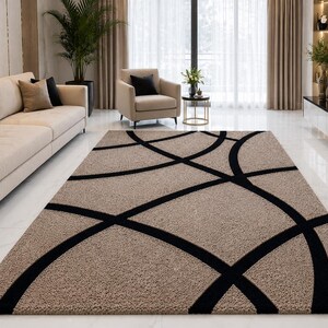 May include: A rectangular area rug featuring a textured beige surface with a bold, black geometric pattern consisting of intersecting curved lines that create large, sweeping circular shapes across the entire length of the floor covering.