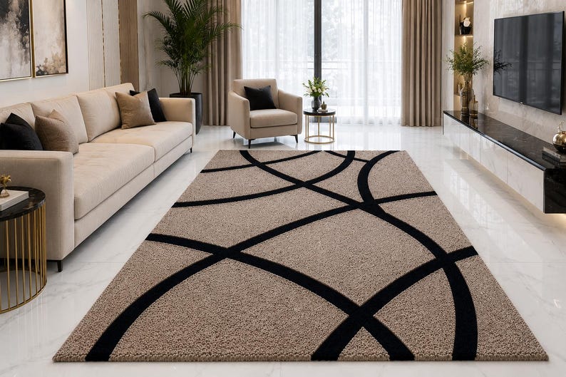 May include: A rectangular area rug featuring a textured beige surface with a bold, black geometric pattern consisting of intersecting curved lines that create large, sweeping circular shapes across the entire length of the floor covering.