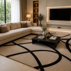 May include: A large rectangular area rug featuring a textured beige pile with a bold, sweeping black circular line pattern. The rug is positioned in a living room setting beneath a dark brown square coffee table and a large beige sectional sofa.