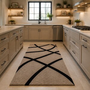 May include: A rectangular area rug featuring a textured beige surface with a bold, black geometric pattern of intersecting curved lines. The rug is positioned centrally on a light-colored floor within a kitchen space with beige cabinetry.