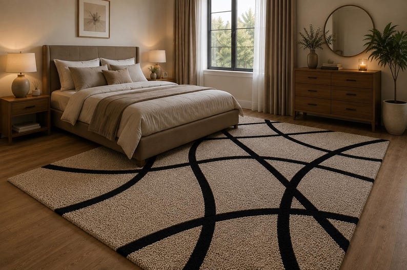May include: A rectangular area rug featuring a textured beige surface with a bold, black, curved line pattern that creates large, intersecting circular shapes across the entire floor covering, positioned in a bedroom setting with neutral furniture.