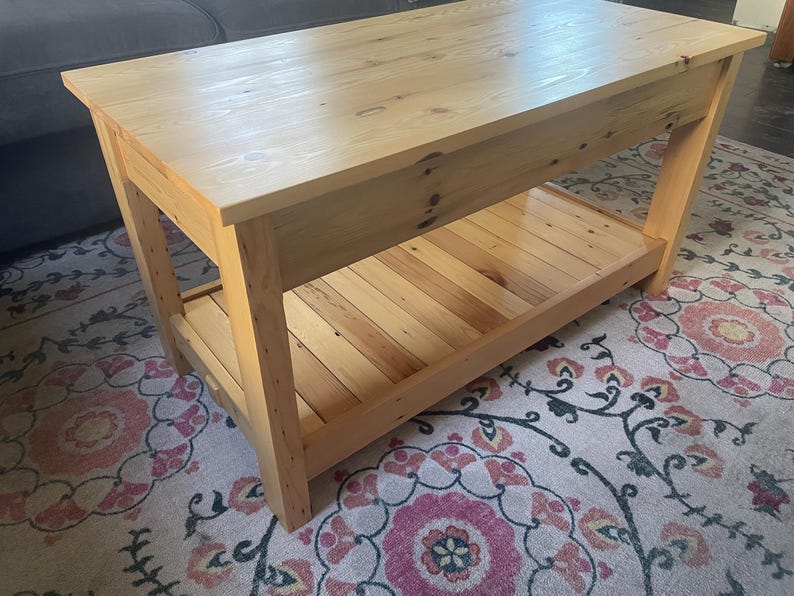 May include: A rectangular coffee table constructed from light-colored natural wood with a smooth top surface and a slatted lower shelf. The table features four sturdy legs and visible wood grain patterns throughout the entire structure.