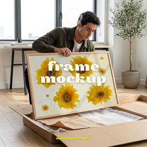 Pode incluir: Uma maquete de moldura retangular com um design de girassol. A moldura é segurada por uma pessoa em uma sala com uma mesa e uma planta. O texto "frame mockup" é exibido na moldura. A moldura está em uma caixa de papelão.