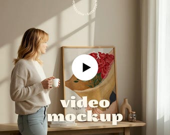 May include: A woman stands near a wooden table, holding a white mug. A framed artwork with red roses is displayed. The words "video mockup" are overlaid on the image, along with the text "motionmockups®".