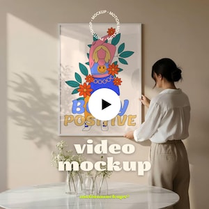 Puede incluir: Una impresión artística enmarcada con las palabras "Body Positive" en una fuente retro. La obra de arte presenta una figura de dibujos animados con flores naranjas y hojas verdes. Se ve a una mujer colgando la impresión enmarcada en una pared beige.