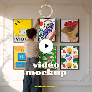 May include: A woman hangs framed art prints on a white wall. The prints feature colorful illustrations, including a smiling face, a tiger, a bouquet of roses, a retro TV, and abstract designs. The text "video mockup" is displayed on the wall.