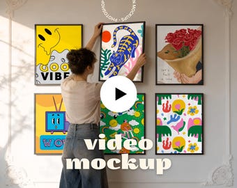 May include: A woman hangs framed art prints on a white wall. The prints feature colorful illustrations, including a smiling face, a tiger, a bouquet of roses, a retro TV, and abstract designs. The text "video mockup" is displayed on the wall.