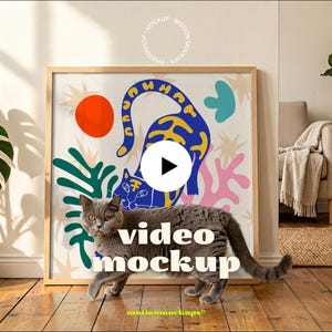 May include: A framed art print with a colorful cat design, featuring a blue cat with yellow accents, a red circle, and green and pink shapes. A gray cat walks in front of the artwork. The words "video mockup" are displayed.