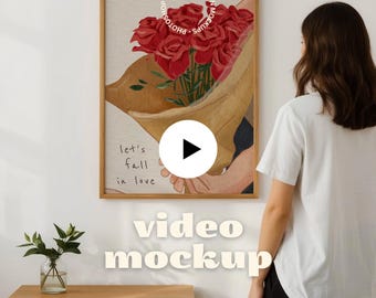 May include: A framed art print featuring a bouquet of red roses in a tan paper wrap. The print includes the text "let's fall in love" and is displayed on a white wall. A woman stands to the right of the print.