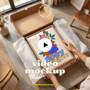 Op de afbeelding: Een ingelijste rechthoekige print in een open kartonnen verzenddoos. De print bevat een gestileerde illustratie van een figuur met oranje bloemen en groene bladeren, met de tekst "BODY POSITIVE" in blauwe en gele letters onderaan.