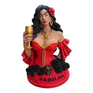 Könnte beinhalten: Eine Büstenfigur einer Frau mit langem schwarzem Haar, die ein rotes Korsett mit Goldbesatz, eine goldene Halskette und goldene Ohrringe trägt. Sie hält einen goldenen Kelch. Der Sockel zeigt schwarze Rosen, einen Totenkopf und den Text PADILHA.