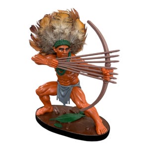 May include: A painted figurine of an archer in a crouching stance, wearing a green headband and a gray loincloth. The figure has a large brown feather headdress, holds a brown bow, and is aiming multiple brown arrows on a brown oval base.