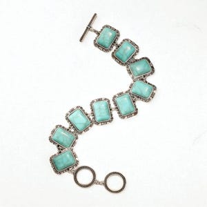 May include: A silver-toned bracelet featuring rectangular turquoise-colored stones. The stones are set in ornate frames and connected by silver links. The bracelet has a toggle clasp for closure. A piece of jewelry.