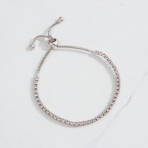 May include: A silver bracelet featuring a line of small, clear gemstones. It has an adjustable slider clasp. The design is simple and elegant. The bracelet is suitable for everyday wear or special occasions.
