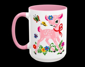 May include: A white ceramic mug with a pink interior and handle. The exterior features a graphic of a pink fawn with a red bow around its neck, surrounded by colorful flowers, green grass, and small butterflies in red, yellow, and blue.
