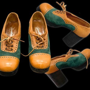 May include: A pair of lace-up shoes featuring a two-tone design with tan leather and dark green suede panels. The shoes have a rounded toe, a thick black block heel, and decorative perforations along the seams. The interior is branded Giardina.