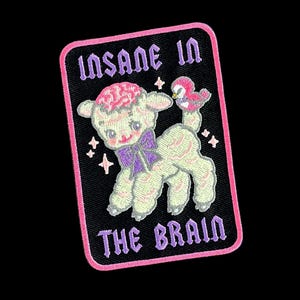 May include: A rectangular embroidered patch with a black background and a pink border. It features a white lamb with a pink brain, a purple bow, and a small bird. The text reads INSANE IN THE BRAIN in purple letters with small white stars.